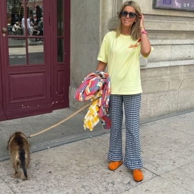 Mulher com roupa colorida e óculos escuros a passear um cão junto a uma porta vermelha