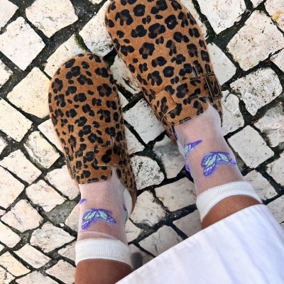Sapatos mule animal print castanhos com meias transparentes e borboletas azuis em calçada portuguesa