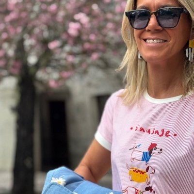Mulher com t-shirt rosa com cães estampados e casaco azul com flores, usando óculos de sol