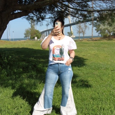 Pessoa com t-shirt branca estampada e calças de ganga com detalhes rendados em branco ao ar livre.