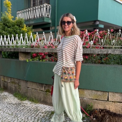 Mulher com calças largas rendadas, camisola às riscas, carteira floral e óculos de sol num passeio urbano.
