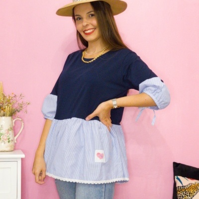 Mulher vestindo túnica azul bicolor com chapéu de palha posando contra parede rosa