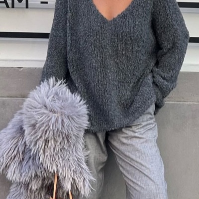 Mulher com camisola cinzenta oversized, calças cinzentas, meias cinzentas, casaco peludo cinzento e mala com padrão Louis Vuitton