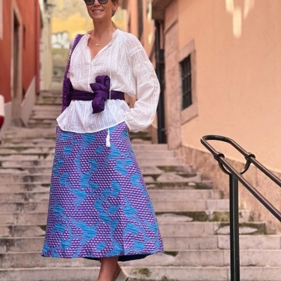 mulher com blusa branca, saia azul e roxa, cinto roxo, óculos escuros, escadaria urbana