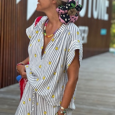 Pessoa com conjunto de roupa listrada com carinhas sorridentes e chapéu rosa com padrão de cães num passadiço de madeira