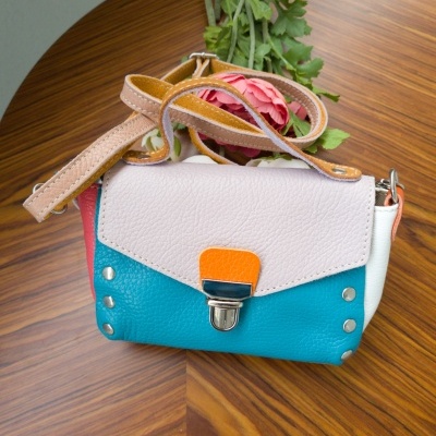 Mala pequena azul turquesa com aba branca e detalhe laranja sobre mesa de madeira