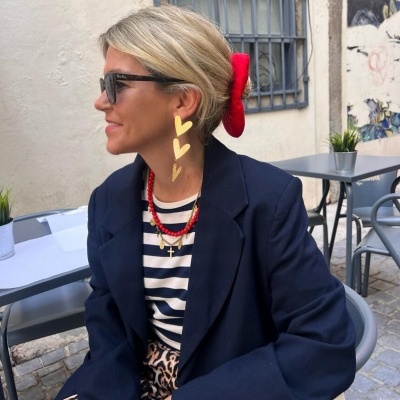Mulher com blazer azul, camisola às riscas, padrão animal print, óculos de sol e acessórios vermelhos e dourados