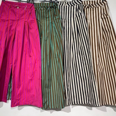 Quatro calças às riscas verticais em várias cores penduradas em cabides.