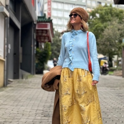 Mulher com roupa colorida numa rua pavimentada, com casaco, saia bordada e boina