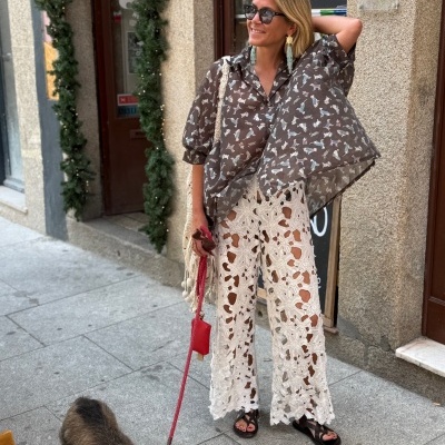 Mulher com camisa castanha com padrão de cães e calças brancas de crochet a passear cão castanho na rua