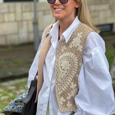 Colete bege bordado com camisa branca e óculos escuros preto ao ar livre