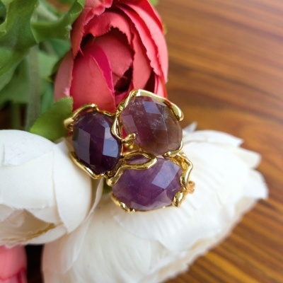 Anel dourado com pedras roxas sobre flores artificiais