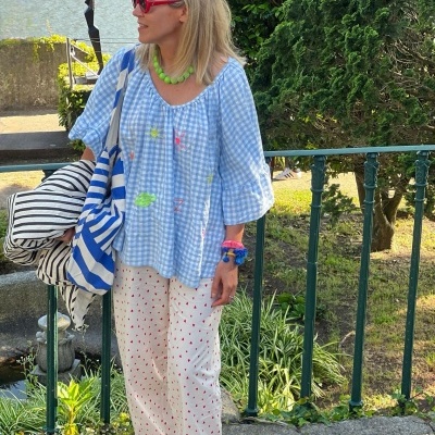 Mulher com túnica azul clara xadrez e calças brancas com corações vermelhos com acessórios coloridos e sacos listrados