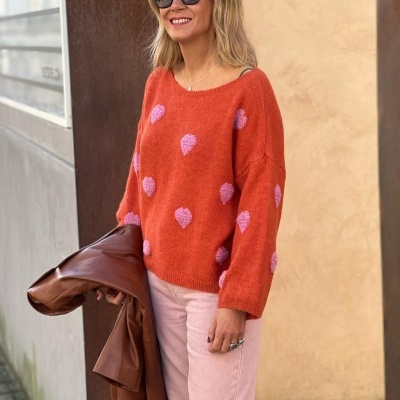 Mulher com camisola laranja com corações rosa e óculos escuros segura casaco castanho