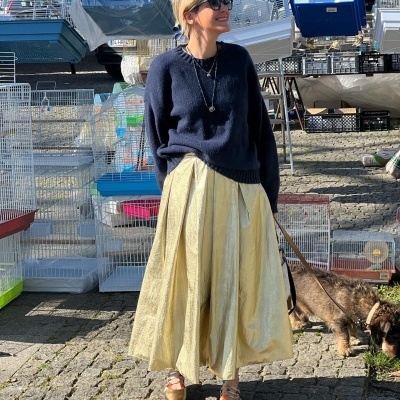 Mulher com camisola azul e saia amarela segurando trela de cão junto a gaiolas sobre calçada