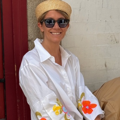 Mulher com camisa branca com flores bordadas, chapéu de palha e óculos escuros