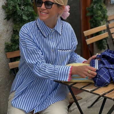 Camisa azul com riscas brancas e detalhes pretos e rosa, ao ar livre, mulher sentada