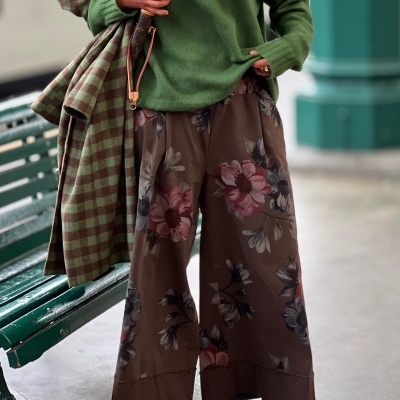 Calças florais largas castanhas com suéter verde, casaco xadrez e cachecol azul