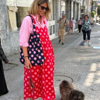 Mulher com vestido vermelho de bolas cor-de-rosa e bolsa azul-marinho com bolas cor-de-rosa, com cão castanho na trela