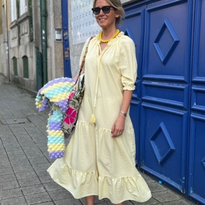 Mulher com vestido amarelo, sapatos roxos e manta tricot colorida em rua