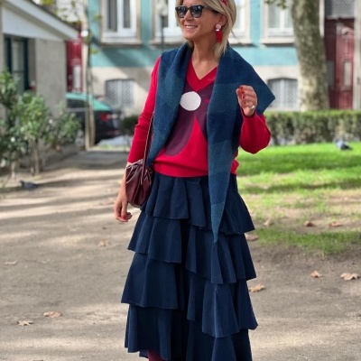 Mulher vestindo saia azul em camadas, camisola vermelha com padrão, lenço azul e óculos de sol