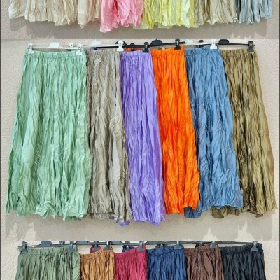 Três fileiras de saias longas franzidas em várias cores penduradas numa parede clara.