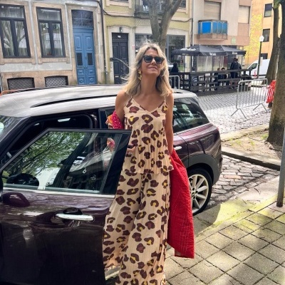 Mulher de vestido comprido de padrão animal print e casaco vermelho junto a carro estacionado na rua