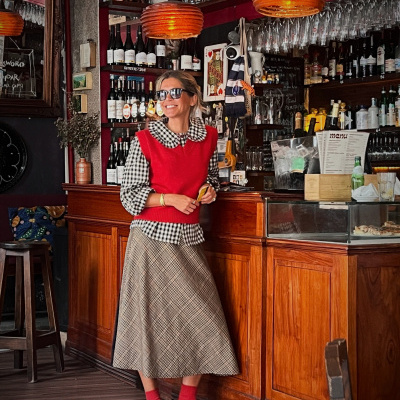 Mulher com blusa xadrez e colete vermelho em cafetaria com barril de vinho