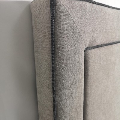 Cabeceira de cama cinzenta com costura escura encostada a parede branca