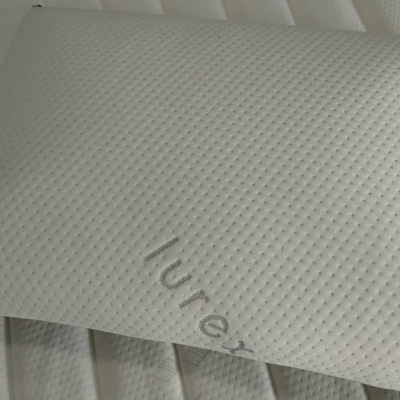 Travesseiro branco texturizado com palavra lurex sobre colchão branco listrado