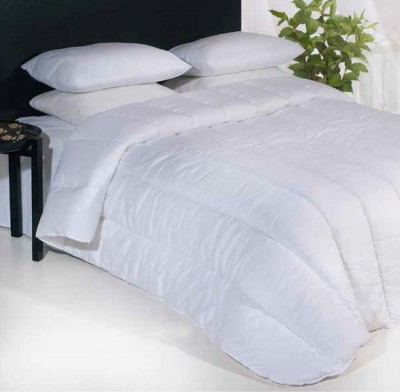 Colcha branca acolchoada em cama com almofadas e planta verde ao fundo