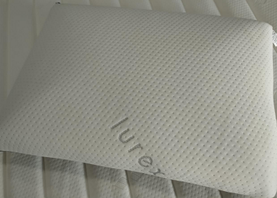 Travesseiro branco texturizado com palavra lurex sobre colchão branco listrado