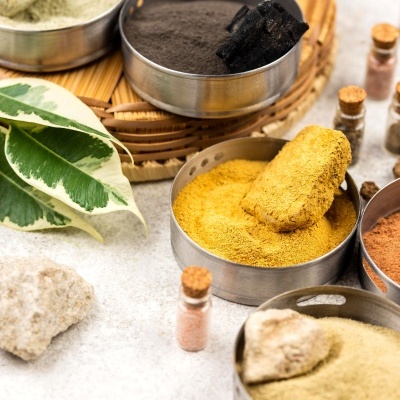 Recipientes metálicos com pós coloridos e enfeites naturais numa superfície clara.