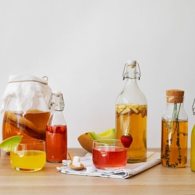 Garrafas e copos de vidro com líquidos coloridos e frutas sobre mesa de madeira clara