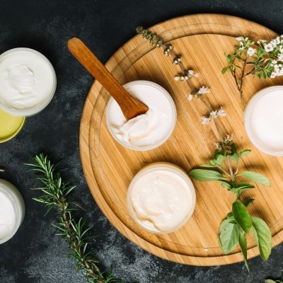 Frascos de creme branco sobre prato de madeira com ervas decorativas