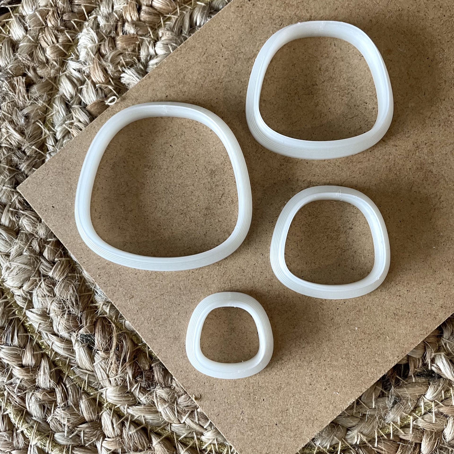 Conjunto de 4 cortadores - BC303 Quatro pulseiras brancas irregulares sobre cartão castanho e esteira entrelaçada
