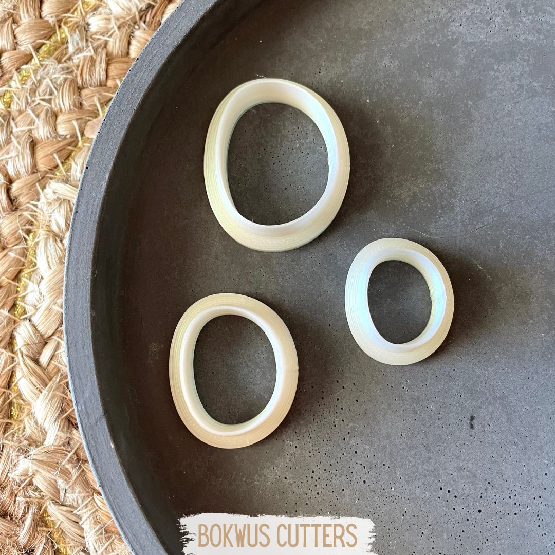 Conjunto de 3 cortadores - BC030 Três cortadores ovais brancos em bandeja preta com etiqueta 'BOKWUS CUTTERS' ao lado