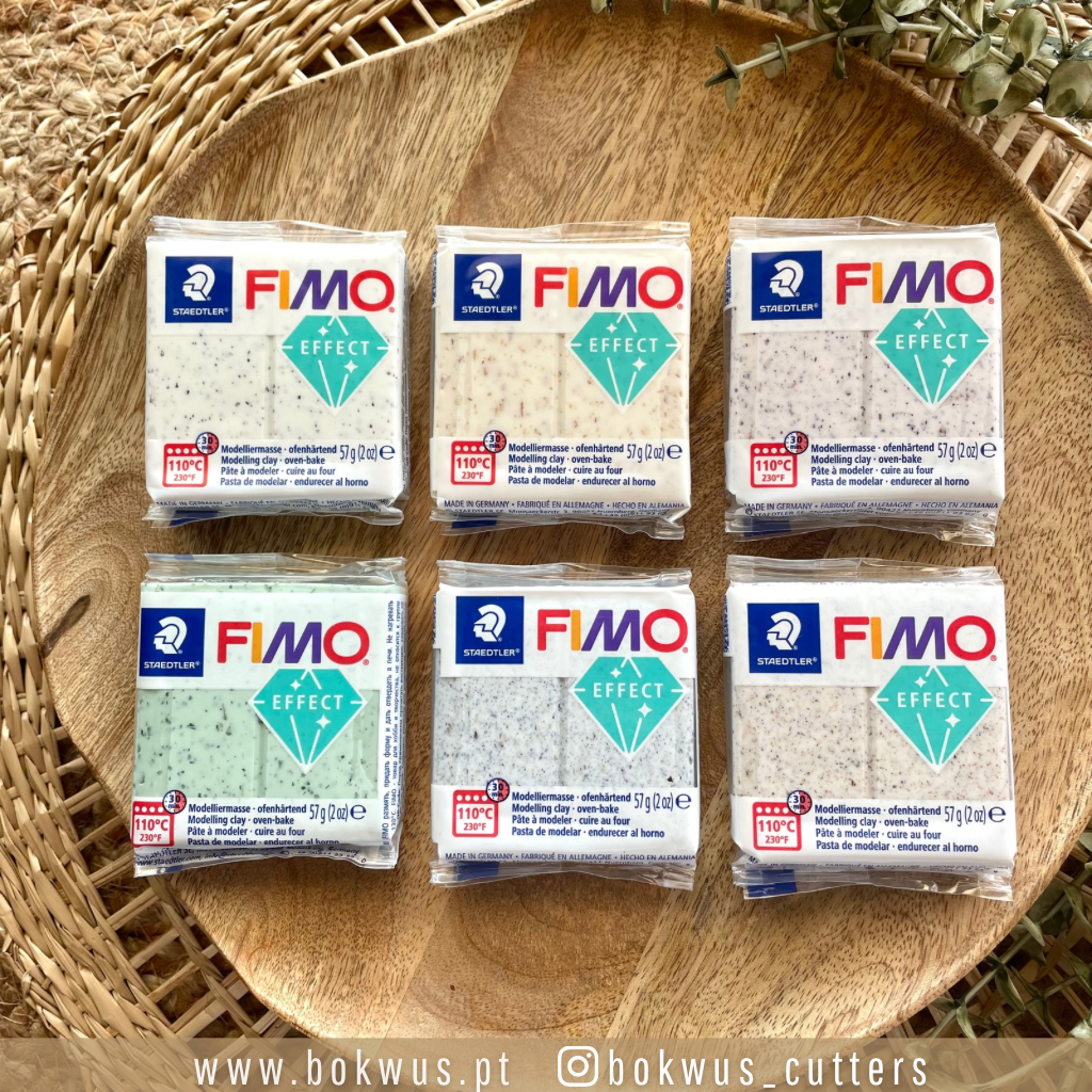 Seis blocos de massa FIMO Effect em várias cores sobre tábua de madeira redonda e cesto de palha