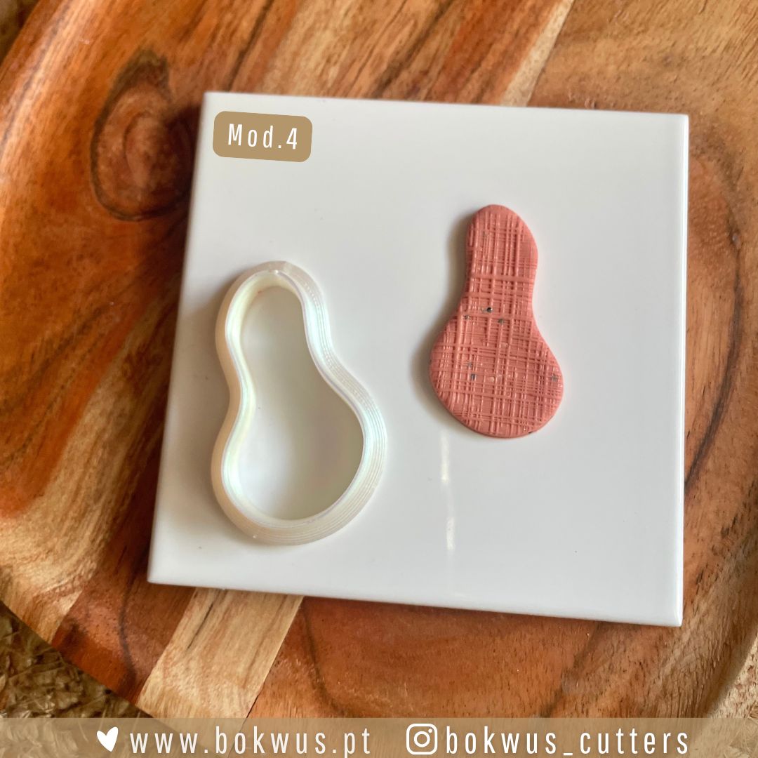 Cortadores formas orgânicas Molde plástico branco e peça de barro vermelho em forma orgânica sobre suporte branco