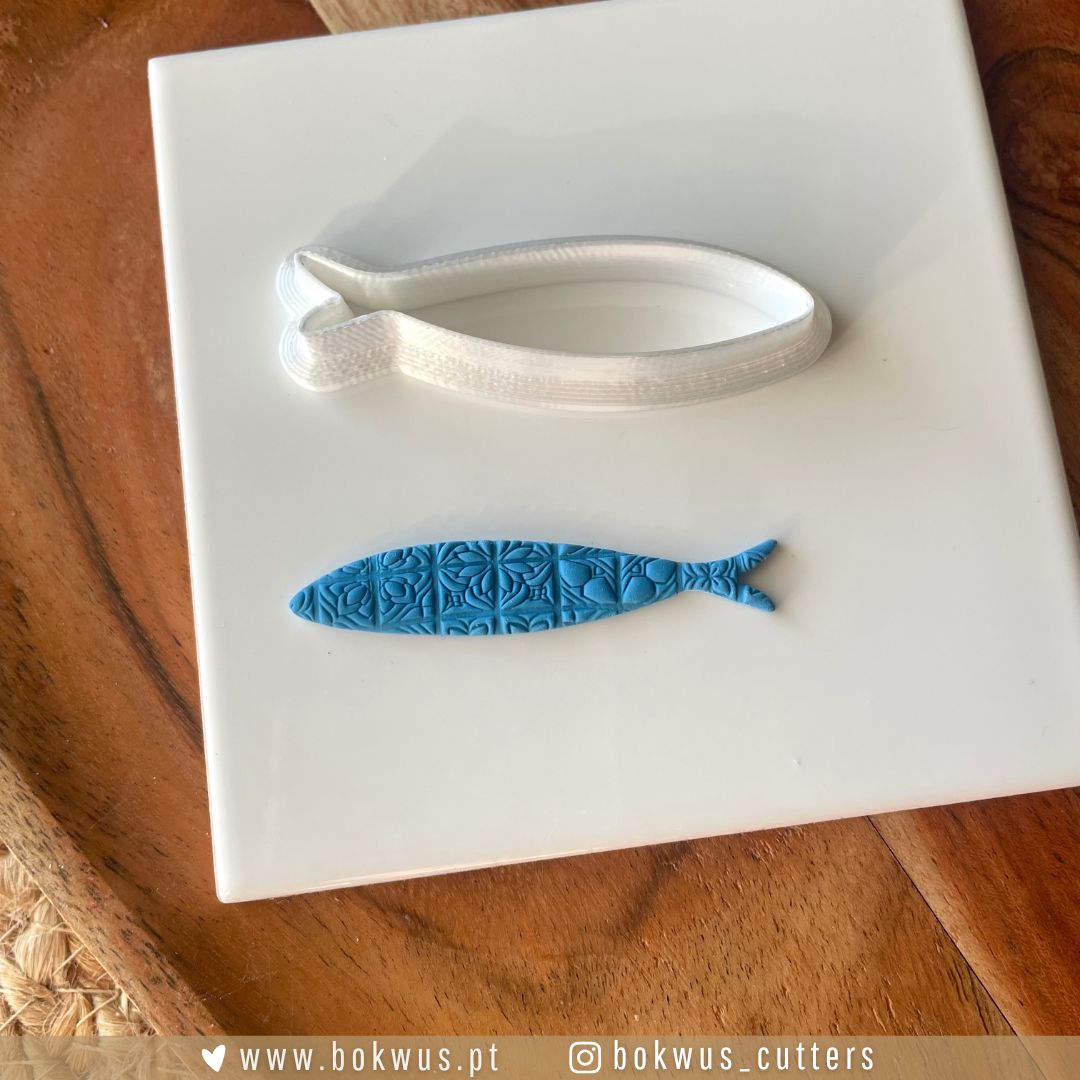 Cortador Sardinha | Disponível em 4 tamanhos Placa branca com forma azul de peixe decorativo e ferramenta branca sobre superfície castanha