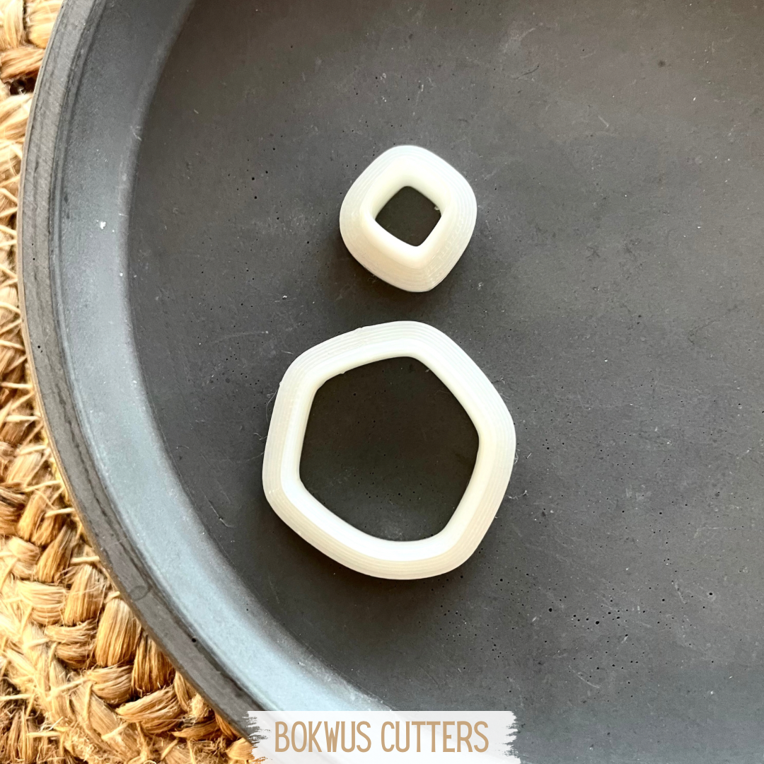 Conjunto de 2 cortadores | BC032 Dois cortadores de plástico branco em formas geometricas sobre tabuleiro preto e superfície de palha