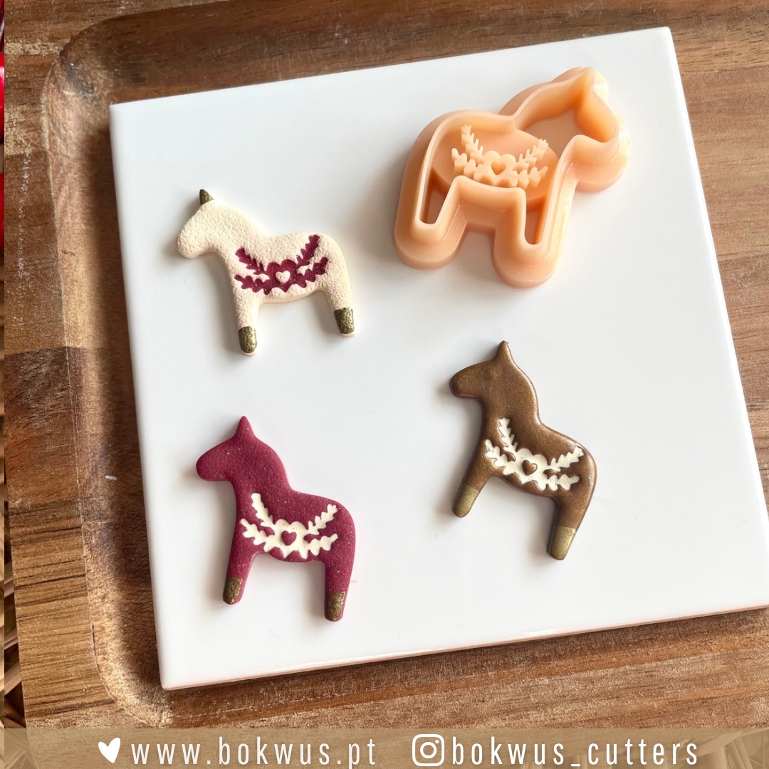 Hygge Noël | Coleção de Natal Três figuras de cavalos coloridos e um cortador de massa em forma de cavalo sobre um prato branco.