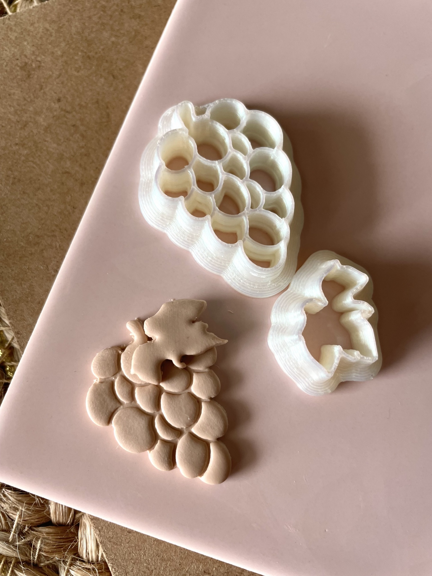 Cortador uvas + folha de videira - BC650 Dois cortadores de massa brancos em forma de uvas e massa em forma de cacho de uvas sobre superfície rosa.