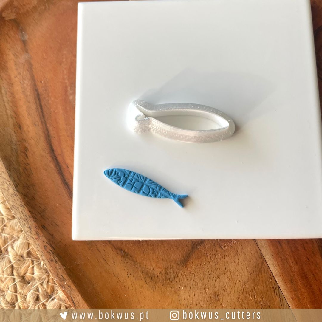 Cortador Sardinha | Disponível em 4 tamanhos Forma de corte metálica em forma de sardinha e molde de silicone azul com textura de escamas numa base branca e madeira