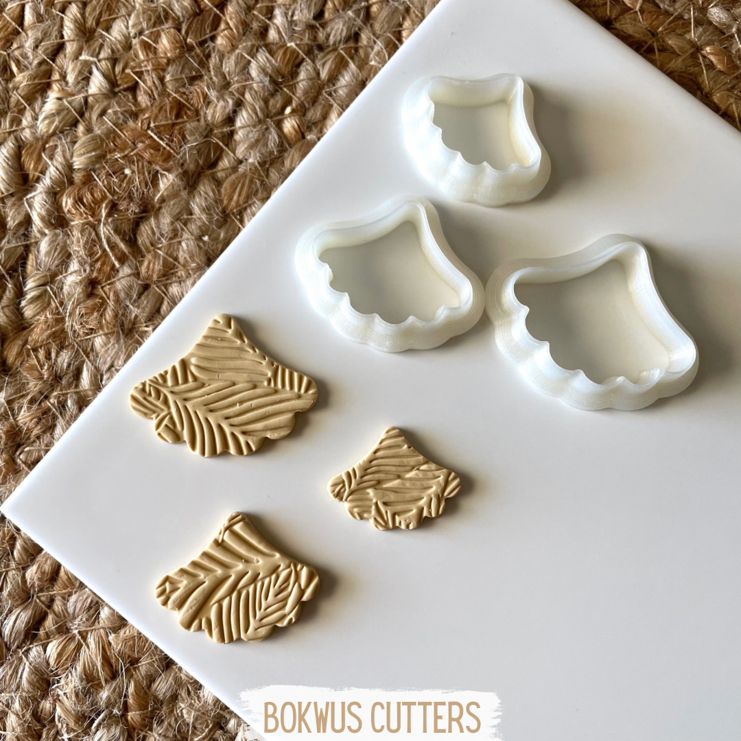 Conjunto de 3 cortadores - BC044 Cortadores de massa brancos e pedaços de massa bege com padrão de folhas num prato branco sobre base de fibras marrons