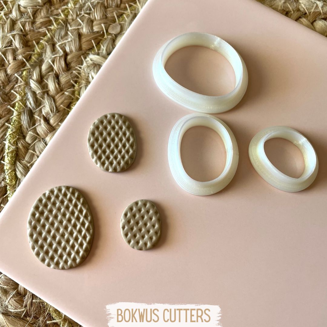 Conjunto de 3 cortadores - BC030 Seis moldes ou cortadores ovais creme e bege texturizados sobre superfície rosa clara e fundo de fibra natural