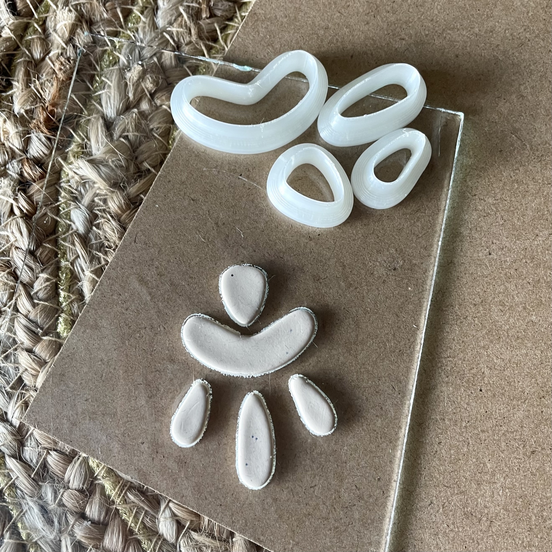 Conjunto de 4 cortadores orgânicos - BC189 Moldes de silicone brancos em formas orgânicas sobre superfície transparente e fundo de corda trançada.