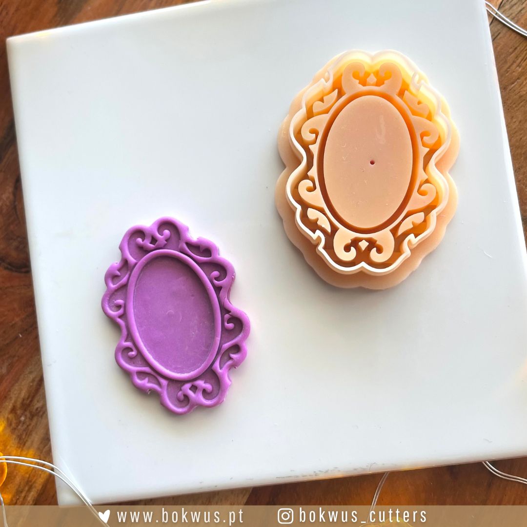 Moldura & Fantasma - Disponível em conjunto ou individualmente Moldes decorativos de cortadores de pasta ou fondant em silicone lilás e material cor de pêssego com padrão ornamentado, sobre placa branca.