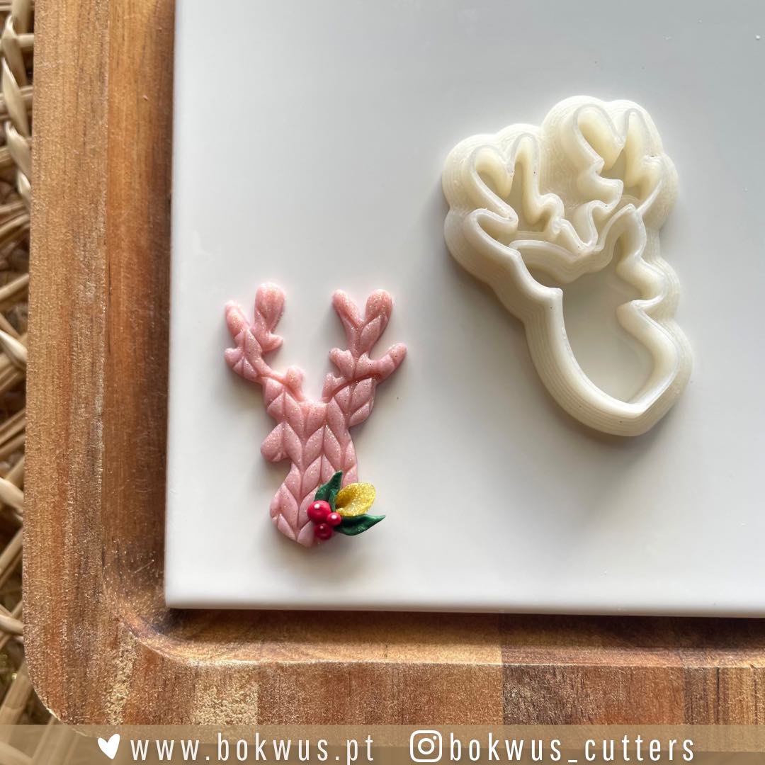 Cortador Veado (4cm) | VERSÃO ESPELHADA | BC1617 Dois moldes de pastelaria de rena, um branco e outro rosa, sobre prato branco e tábua de madeira.