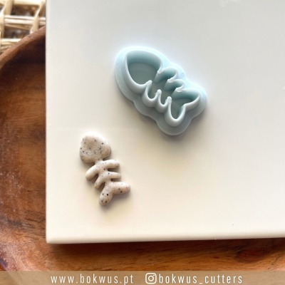 Cortadores de biscoitos em silicone azul claro em forma de esqueleto com coração e peça de massa branca com pontilhados pretos sobre superfície branca e madeira